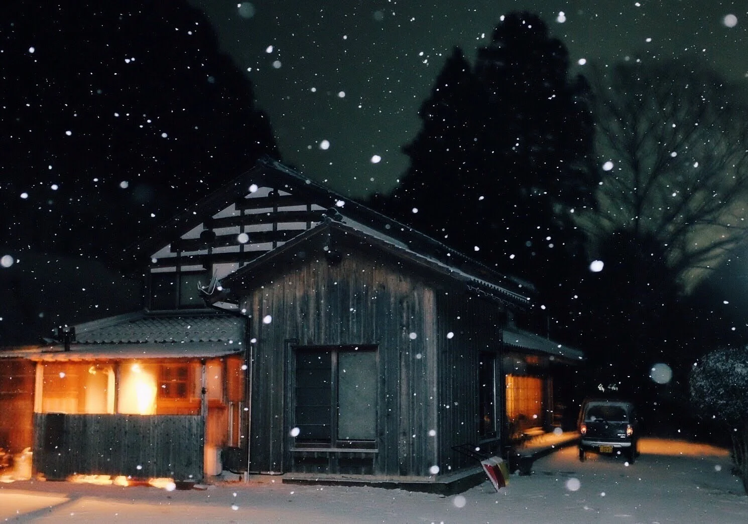 雪が舞う夜、灯りのともった古民家